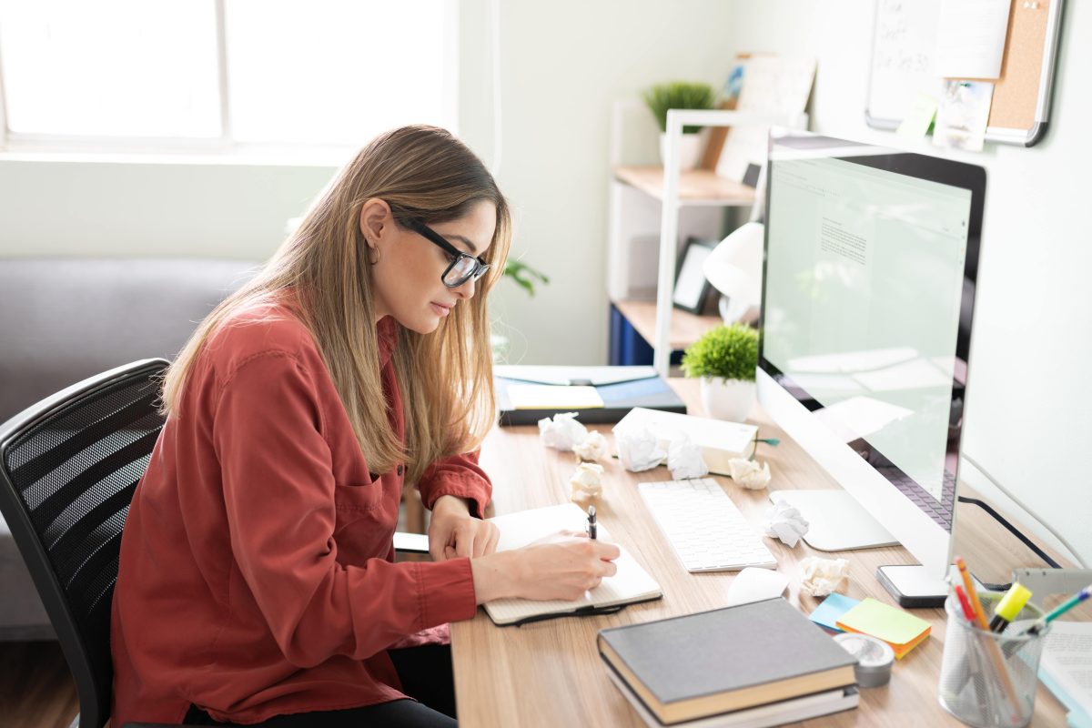 female writer taking notes while writing a document on her computer